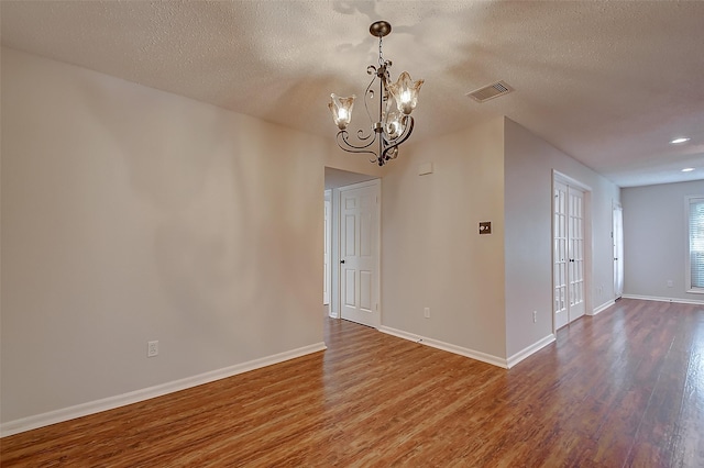 unfurnished dining area with a chandelier, a textured ceiling, wood finished floors, visible vents, and baseboards