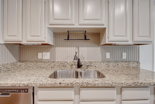 kitchen featuring light stone countertops, stainless steel dishwasher, white cabinetry, and a sink