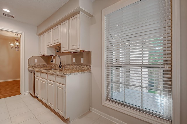 kitchen featuring a sink, white cabinetry, baseboards, visible vents, and light stone countertops