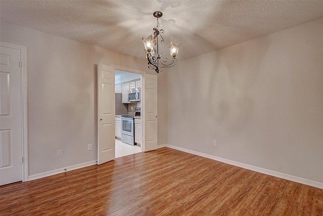 unfurnished room with a chandelier, a textured ceiling, light wood-style flooring, and baseboards