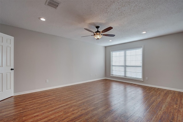 spare room featuring dark wood-type flooring, visible vents, a textured ceiling, and baseboards