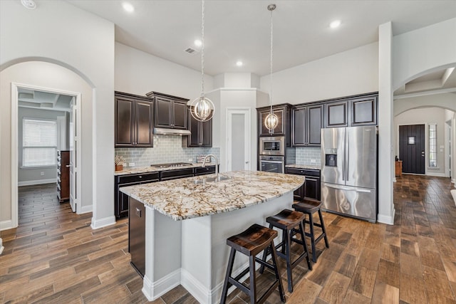 kitchen with stainless steel appliances, arched walkways, dark wood finished floors, and a sink