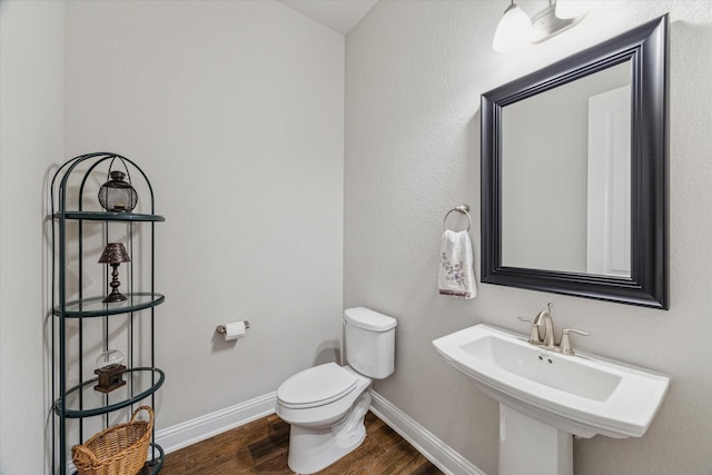 half bath featuring a sink, wood finished floors, toilet, and baseboards