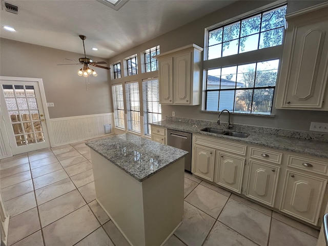 kitchen featuring light stone counters, a sink, visible vents, wainscoting, and dishwasher