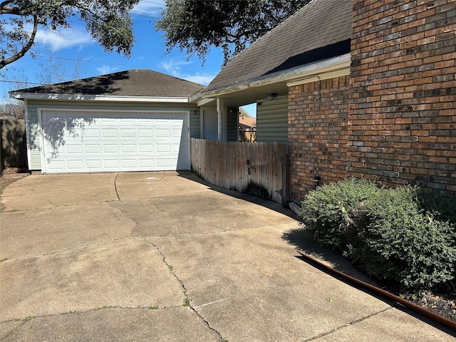 view of side of property with driveway, a garage, fence, and roof with shingles