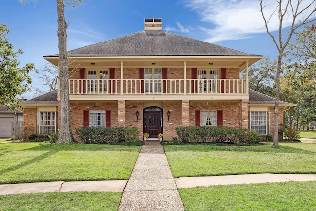 view of front facade featuring a balcony, a front yard, and brick siding