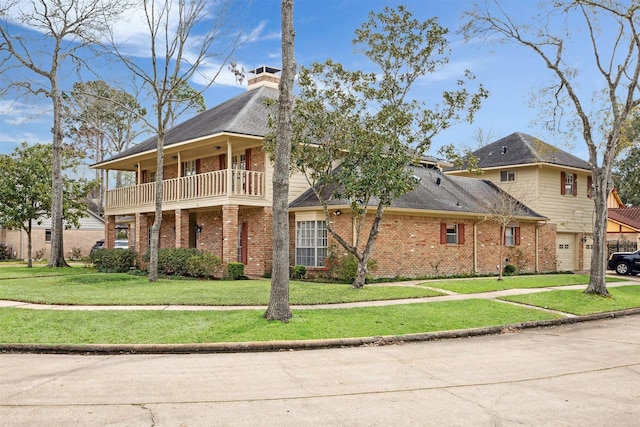 view of front of property with a balcony, a garage, brick siding, a chimney, and a front yard