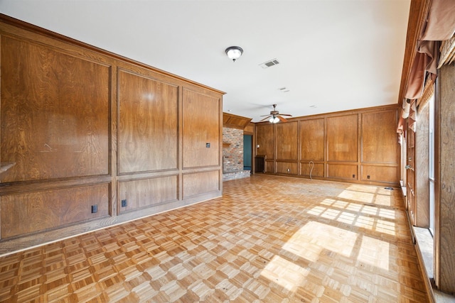 empty room with ceiling fan, wood walls, visible vents, and a decorative wall