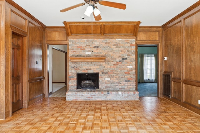 unfurnished living room featuring ceiling fan, wooden walls, a fireplace, and crown molding