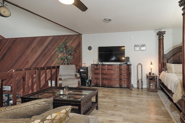 living room featuring ceiling fan, light wood-type flooring, visible vents, and wooden walls