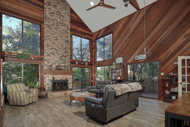 living room with high vaulted ceiling, light wood-type flooring, a fireplace, and wooden walls