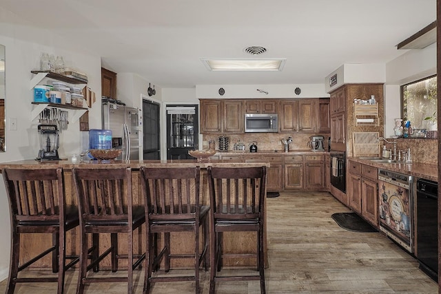 interior space featuring a breakfast bar area, a sink, light wood-style floors, black appliances, and tasteful backsplash