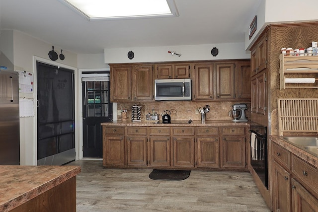 kitchen featuring appliances with stainless steel finishes, decorative backsplash, and light wood finished floors