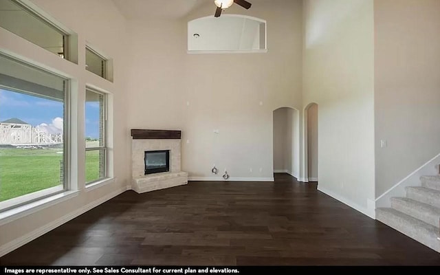 719 Woodbinde Dr, League City, TX 77573 - unfurnished living room featuring ceiling fan, a stone fireplace, a towering ceiling, baseboards, and dark wood finished floors