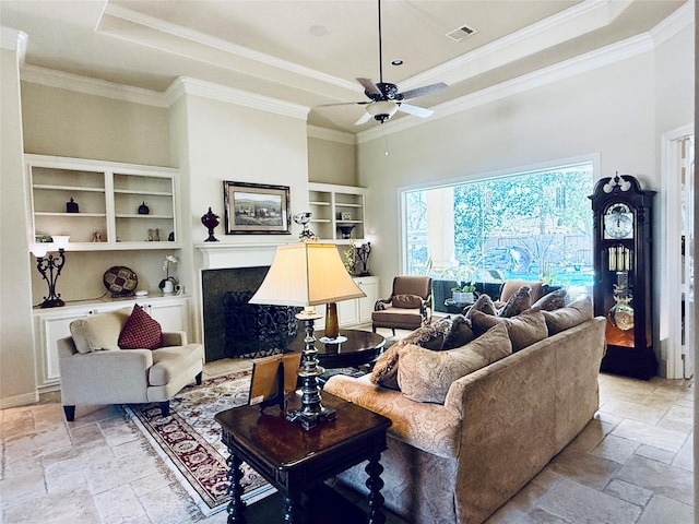 living area with built in features, visible vents, a raised ceiling, a premium fireplace, and stone tile flooring