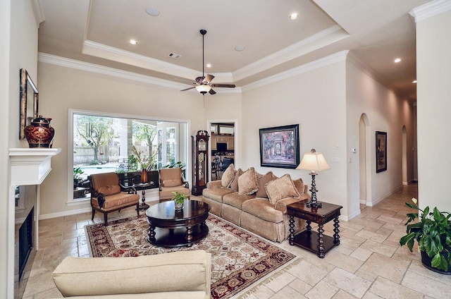 living area featuring stone tile floors, baseboards, a raised ceiling, ornamental molding, and a fireplace