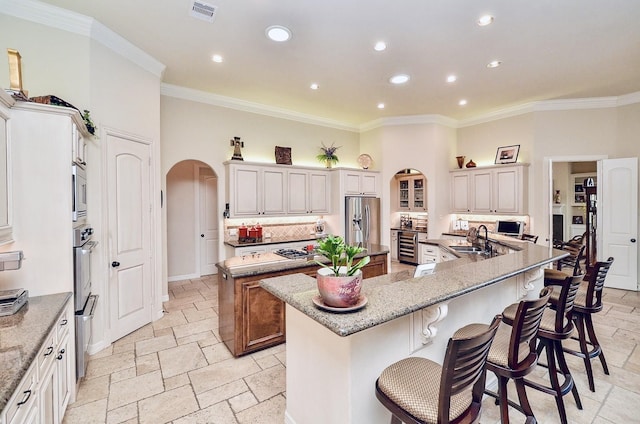 kitchen with appliances with stainless steel finishes, arched walkways, stone tile flooring, and a large island with sink