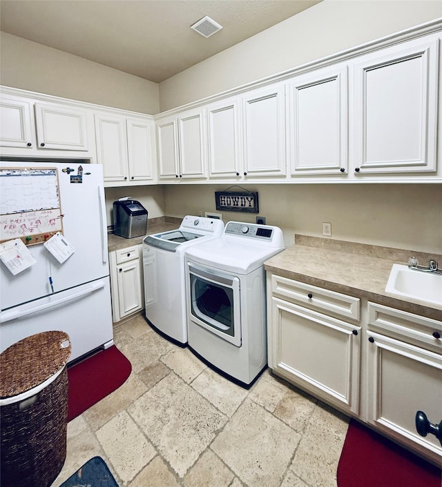 laundry area with washing machine and clothes dryer, stone tile flooring, cabinet space, visible vents, and a sink