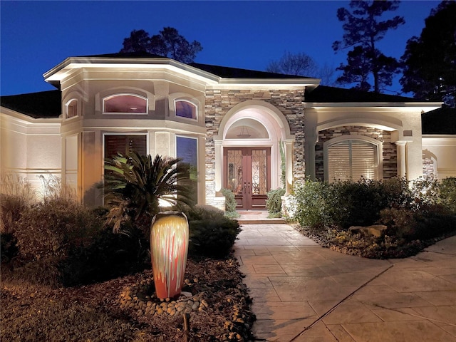 exterior entry at twilight featuring stone siding, french doors, and stucco siding