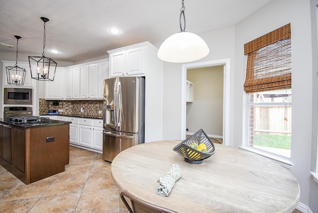 kitchen featuring white cabinetry, appliances with stainless steel finishes, backsplash, dark countertops, and decorative light fixtures