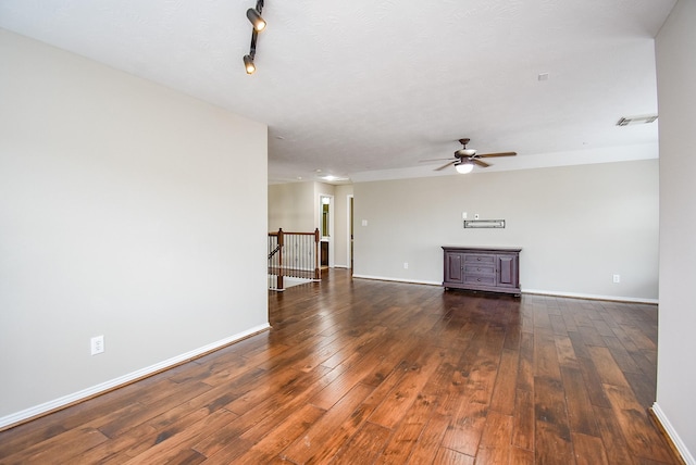 unfurnished living room with dark wood-type flooring, a ceiling fan, visible vents, baseboards, and rail lighting