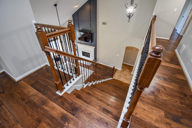 stairs featuring arched walkways, a fireplace, a notable chandelier, wood finished floors, and baseboards