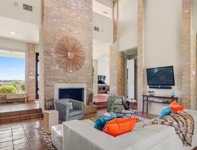 living area with visible vents, brick wall, a fireplace, and a towering ceiling