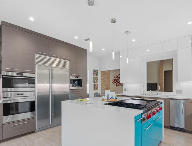 kitchen featuring high quality appliances, a center island, hanging light fixtures, light countertops, and white cabinetry