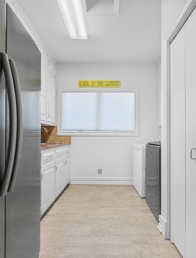 kitchen with light wood finished floors, white cabinets, washer and clothes dryer, stainless steel refrigerator, and backsplash