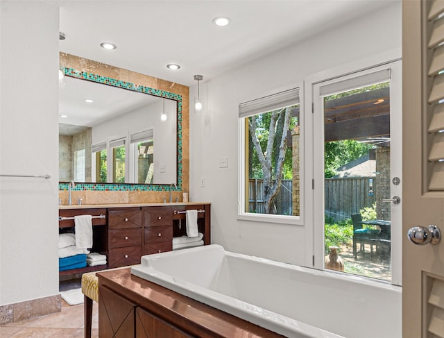 bathroom featuring a healthy amount of sunlight, a soaking tub, recessed lighting, and vanity