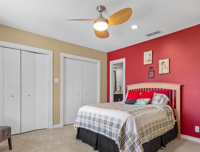 bedroom with a ceiling fan, visible vents, multiple closets, and light colored carpet