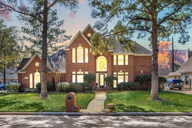 view of front of house featuring roof with shingles, a front yard, and brick siding