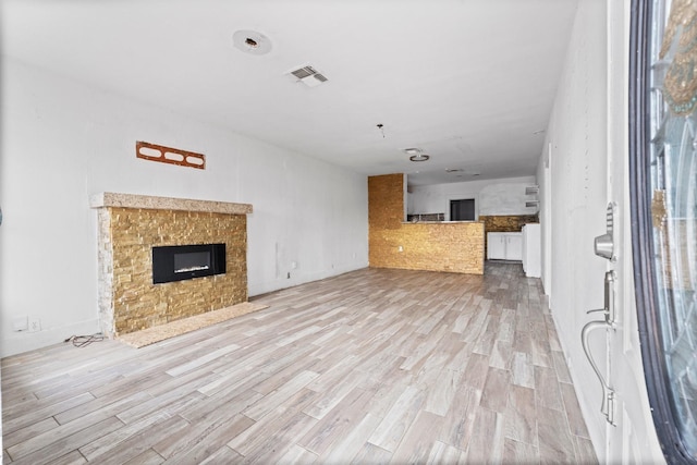 unfurnished living room with visible vents, light wood-style flooring, and a tiled fireplace