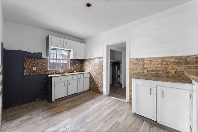 kitchen featuring decorative backsplash, electric water heater, light wood-style floors, white cabinetry, and a sink