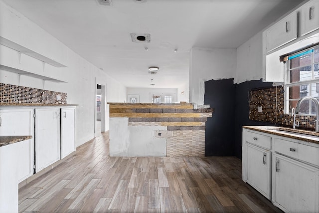 kitchen with light wood finished floors, tasteful backsplash, white cabinetry, and a sink