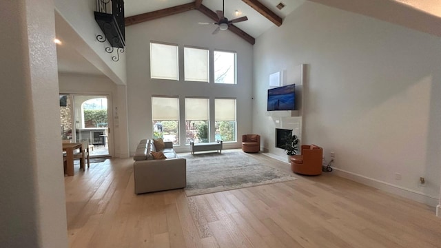 unfurnished living room with visible vents, a glass covered fireplace, light wood-style flooring, high vaulted ceiling, and beam ceiling