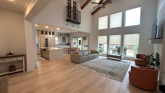 living area featuring light wood-style flooring, a fireplace, a towering ceiling, a ceiling fan, and beamed ceiling