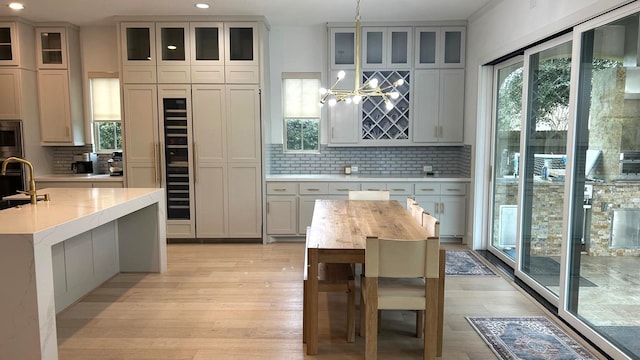 kitchen with pendant lighting, a center island with sink, glass insert cabinets, a sink, and light wood-type flooring