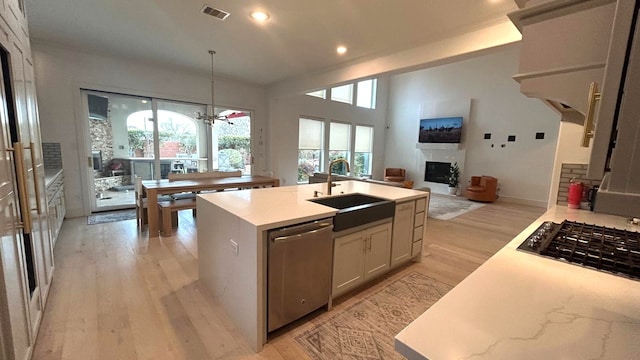 kitchen featuring visible vents, an island with sink, decorative light fixtures, stainless steel dishwasher, and a sink