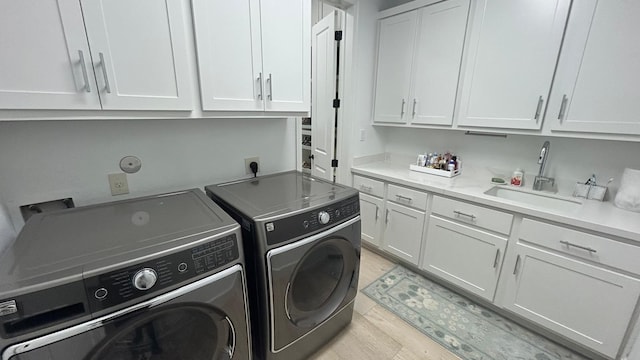 laundry area featuring light wood-style floors, washing machine and dryer, cabinet space, and a sink