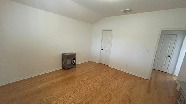 empty room with lofted ceiling, light wood finished floors, visible vents, and baseboards