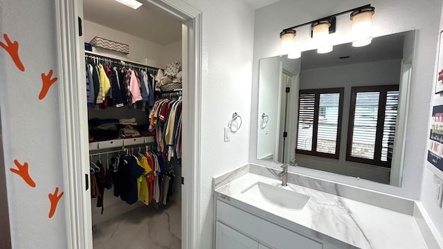 bathroom with marble finish floor, a spacious closet, and vanity