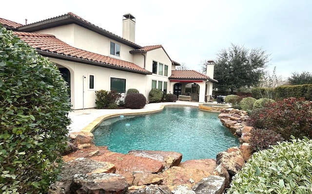 rear view of house featuring a tile roof, a chimney, stucco siding, a pool with connected hot tub, and a patio area