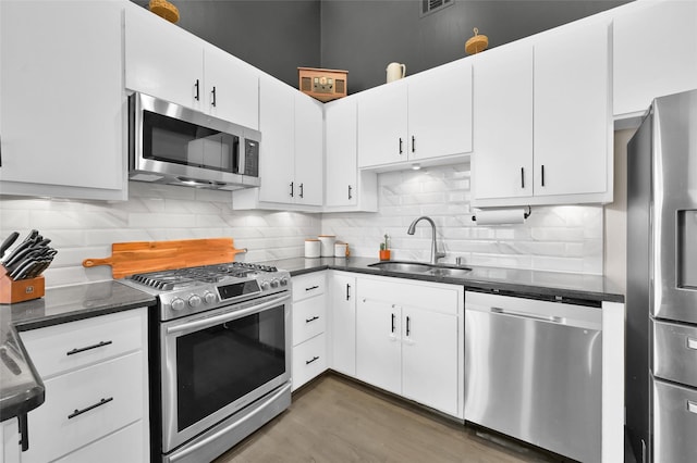 kitchen with stainless steel appliances, dark countertops, decorative backsplash, white cabinets, and a sink