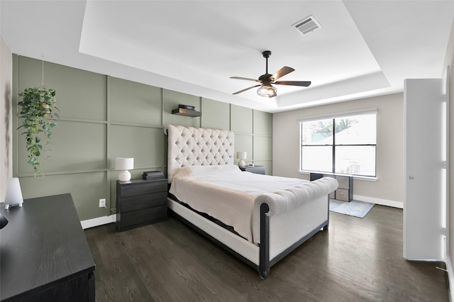 bedroom featuring a tray ceiling, visible vents, a decorative wall, dark wood-type flooring, and baseboards