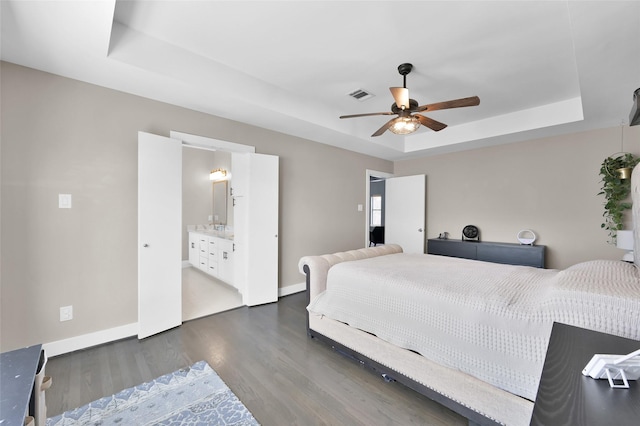 bedroom with a tray ceiling, dark wood finished floors, visible vents, a ceiling fan, and baseboards