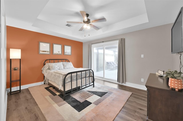 bedroom featuring a tray ceiling, wood finished floors, and access to exterior