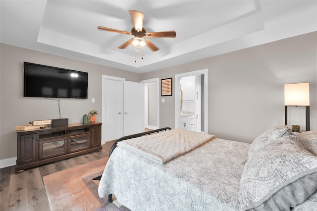 bedroom featuring a tray ceiling, dark wood-style flooring, ceiling fan, and ensuite bathroom