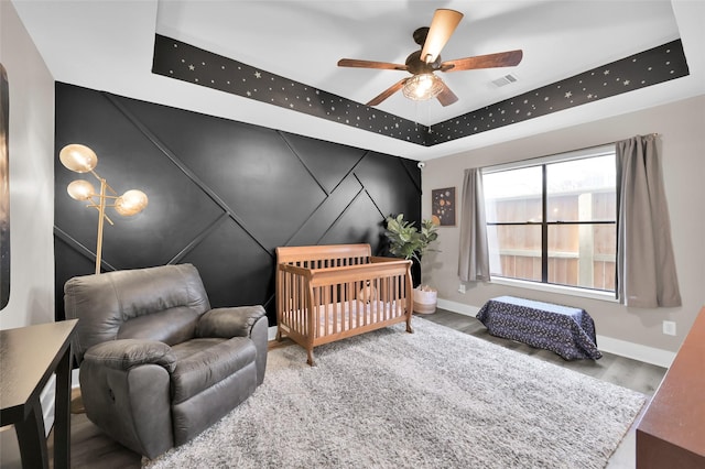 bedroom featuring wood finished floors, a ceiling fan, visible vents, baseboards, and a raised ceiling