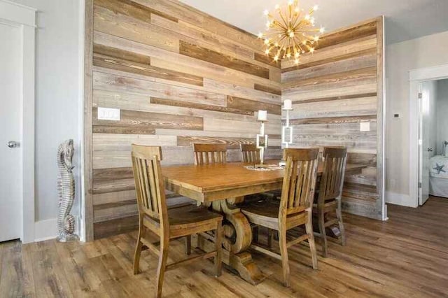 dining room with wood finished floors, wood walls, baseboards, and an inviting chandelier